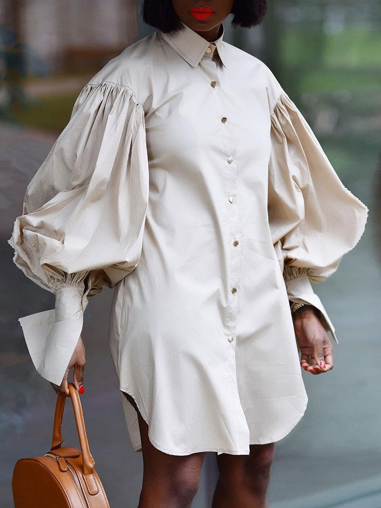 Woman wearing a beige oversized shirt dress with dramatic balloon sleeves and a round tan handbag.