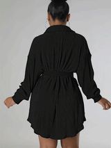 Woman wearing a black pleated shirt dress over denim shorts