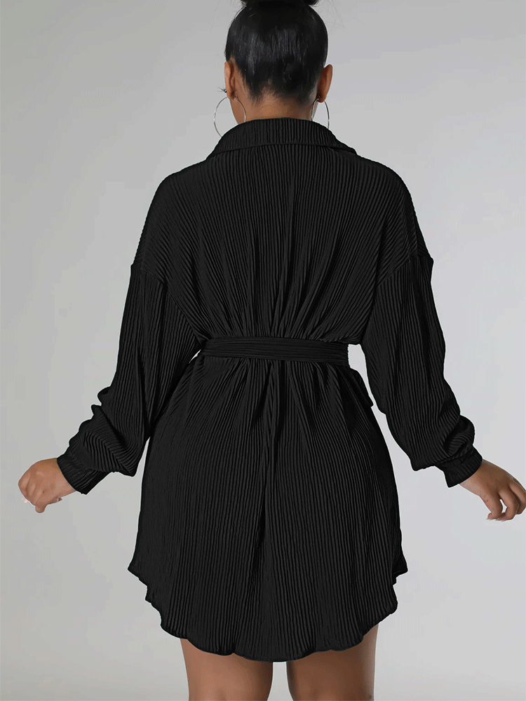 Woman wearing a black pleated shirt dress over denim shorts