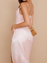 Side view of a woman wearing a light pink satin midi dress with a high slit.