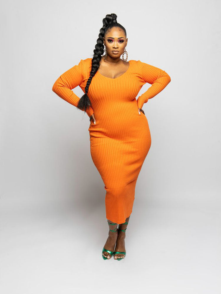 Woman in an orange ribbed knit midi dress with long sleeves and a V-neckline, posing with hands on hips and a braid.