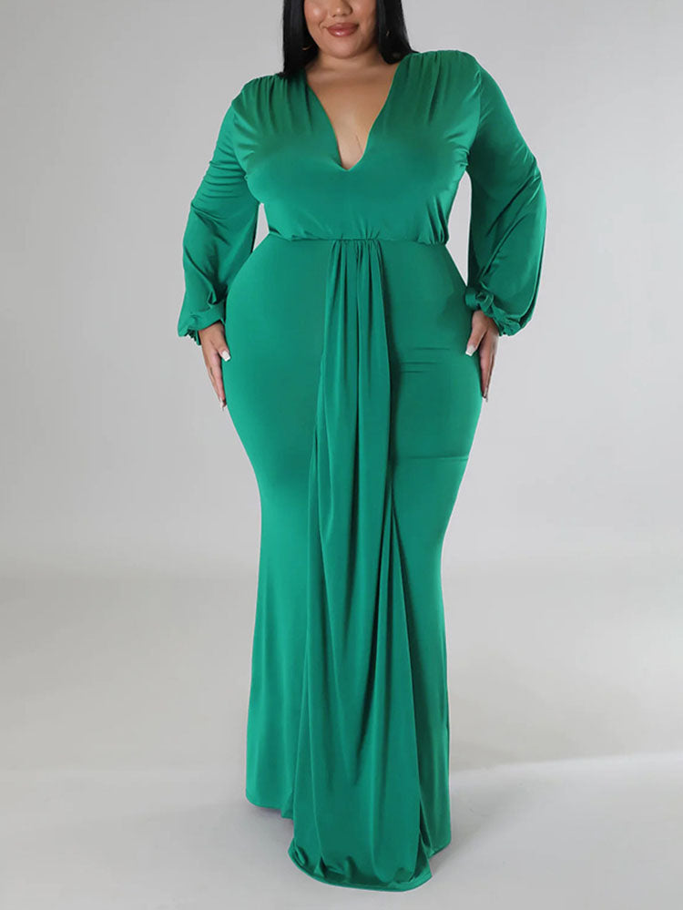 Woman wearing a green, floor-length, long-sleeved gown with a V-neckline and draped skirt