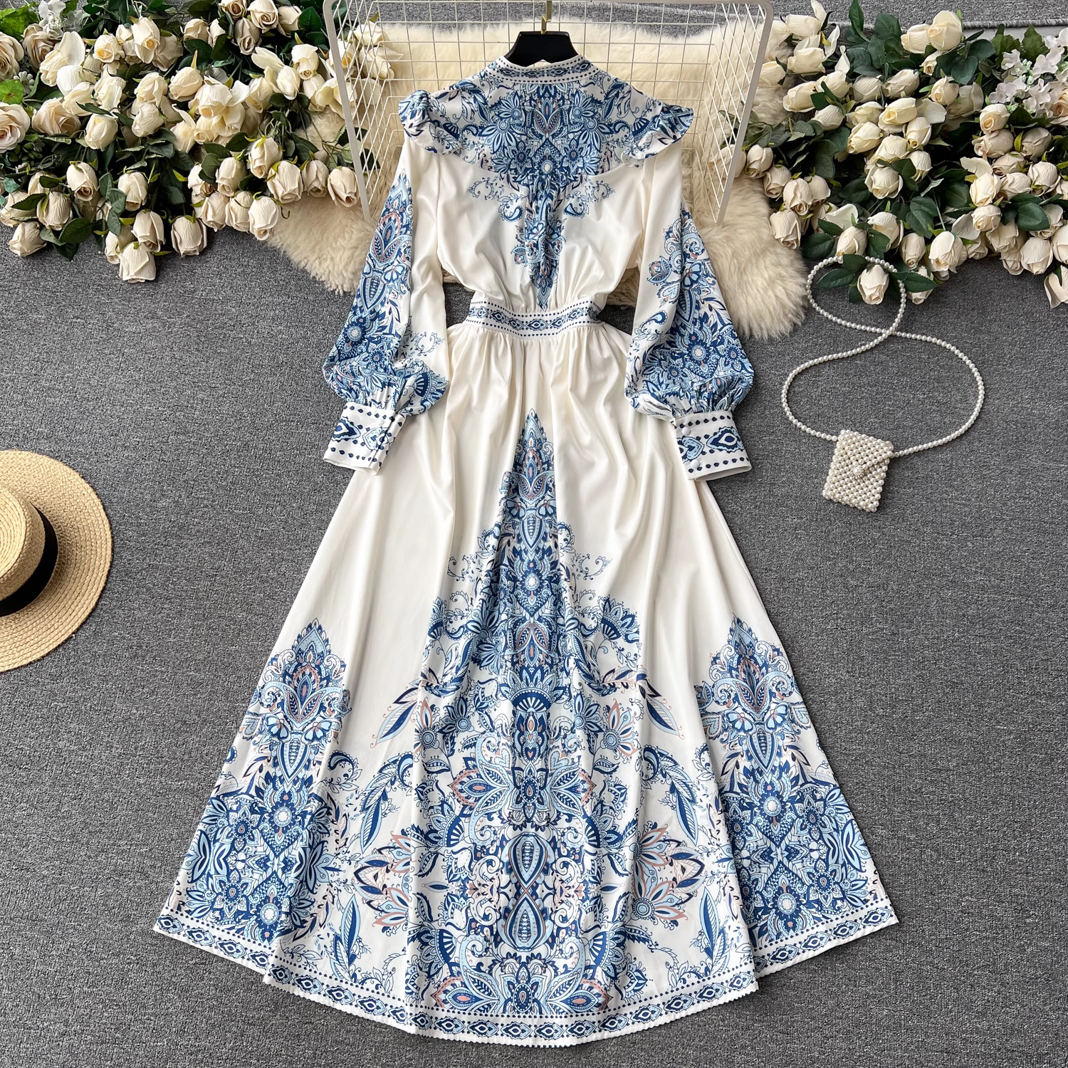 Overhead view of the white maxi dress with blue paisley print, positioned alongside a straw hat and a pearl-adorned handbag.