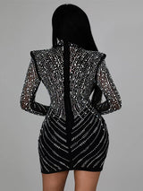 Back view of a woman in a black long-sleeved mini dress with intricate rhinestone patterns. The dress is form-fitting and showcases a central seam.