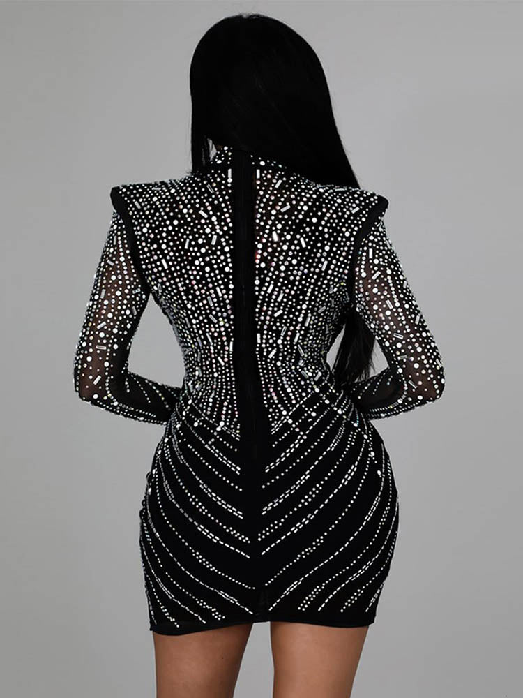 Back view of a woman in a black long-sleeved mini dress with intricate rhinestone patterns. The dress is form-fitting and showcases a central seam.