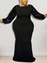 Woman wearing a black floor-length dress with sequined long puff sleeves and a round neckline.