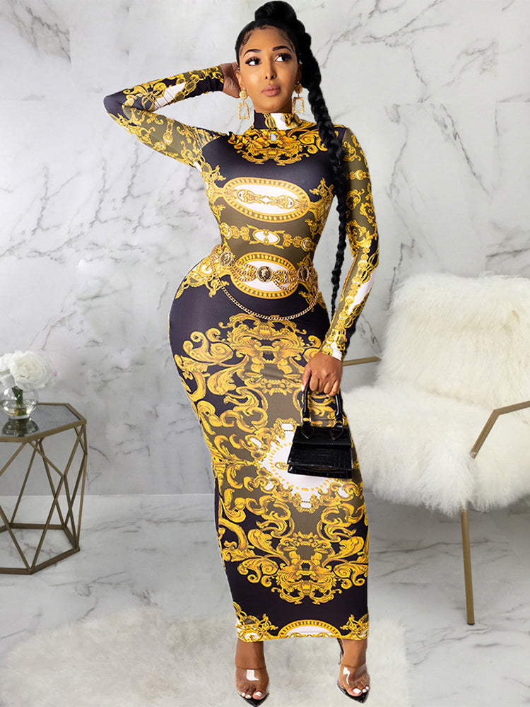 Woman wearing a long-sleeved, baroque-print maxi dress with a high neckline and a belted waist, standing against a marble backdrop.