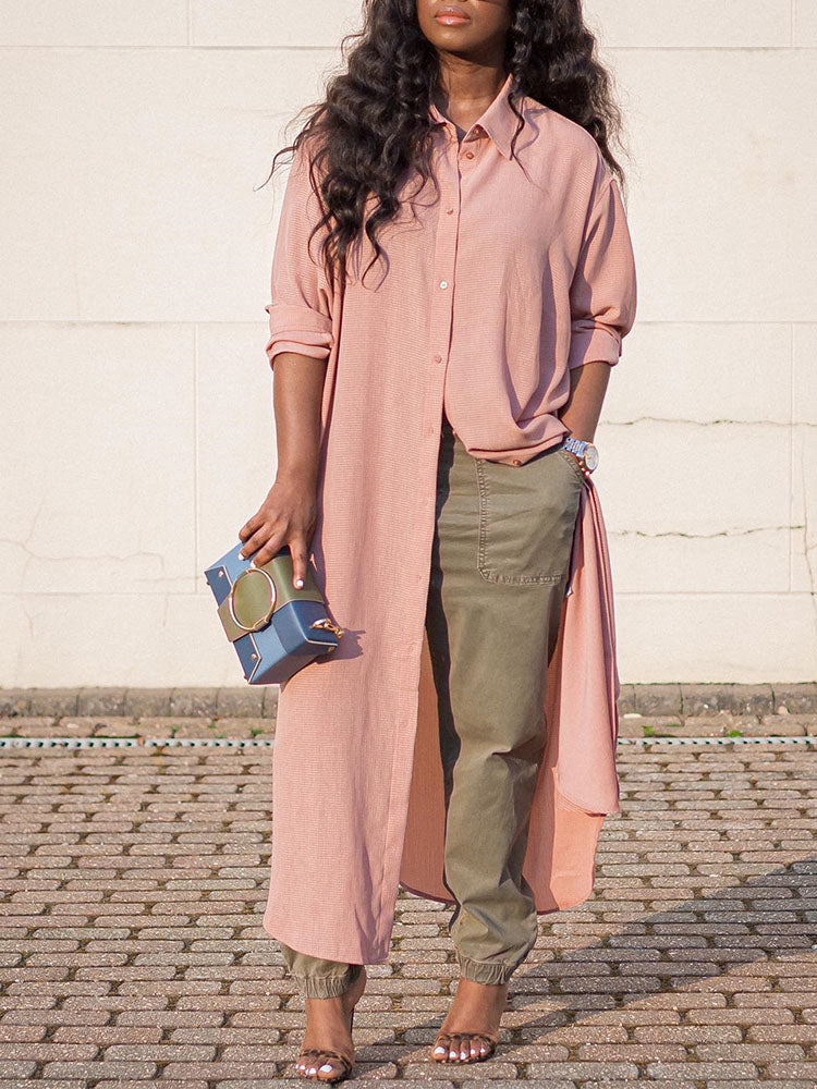 Woman wearing a long pink collared shirt dress over olive green cargo pants and heels, holding a blue and green clutch.