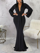 Woman wearing a floor-length black formal dress with bishop sleeves and a deep V-neck.
