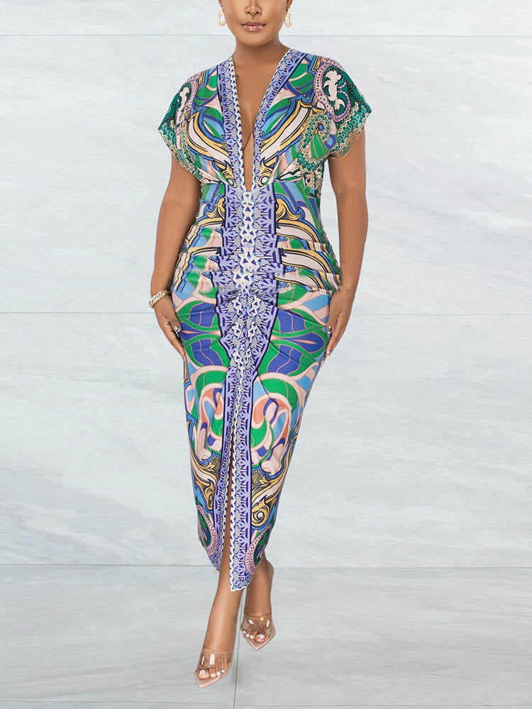 Front view of a woman in a colorful abstract print V-neck midi dress with a high slit, standing against a marble-patterned wall.