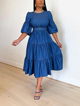 Woman wearing a blue denim midi dress with puff sleeves and a tiered skirt