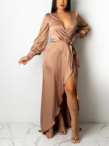 Woman wearing a champagne satin wrap maxi dress with a high slit and long puff sleeves, posing against a white wall.