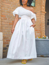 Woman wearing a white one-shoulder maxi dress with puff sleeves and cut-out details, paired with yellow sandals.