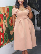 Woman wearing a light pink off-the-shoulder belted dress with puff sleeves and a pleated midi skirt, standing in front of a colorful geometric mural.
