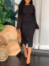 Woman wearing a black sheath dress with cape sleeves and a slit hem.