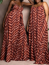 Two women wearing similar brown and white tie-dye print maxi dresses, one with a belted waist, standing against a textured brown wall.