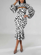 Woman wearing a black and white leopard print knit dress with a high neck, cut-out detail, long puff sleeves, and a mermaid hemline, posing with arms raised.