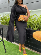 Woman wearing a black one-shoulder dress with a pleated sleeve and a tan clutch