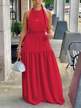 Woman wearing a red halter neck maxi dress with an elasticated waist and tiered skirt, holding a white clutch bag.