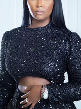 Close-up of the bodice of a black sequined dress showing the high neckline, long sleeves, and waist cut-out.