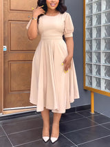 Woman wearing a beige A-line dress with puff sleeves and a round neckline.