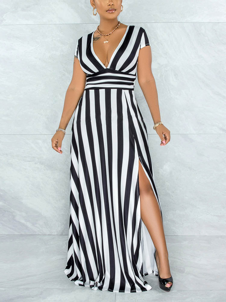 Woman wearing a black and white striped maxi dress with a V-neck and high slit, standing against a marble wall.