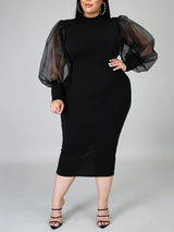 Plus-size woman wearing a black mock neck sheath dress with sheer puff sleeves and a slit hem, front view