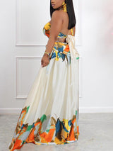 side view of a woman wearing a cream colored abstract print halter neck maxi dress with cut-out details and a side slit