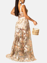 Back view of a woman in a sheer floral embroidered maxi dress with a corset-style bodice.