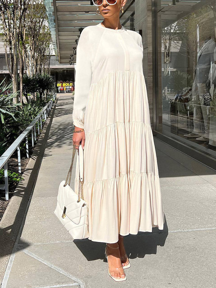 Woman wearing a long, cream-colored tiered maxi dress with long sleeves and a white handbag.