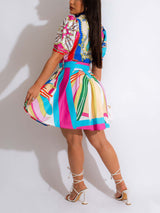 Rear view of a woman in a white short-sleeve dress with a colorful abstract print, showing the pleated skirt and lace-up heels.