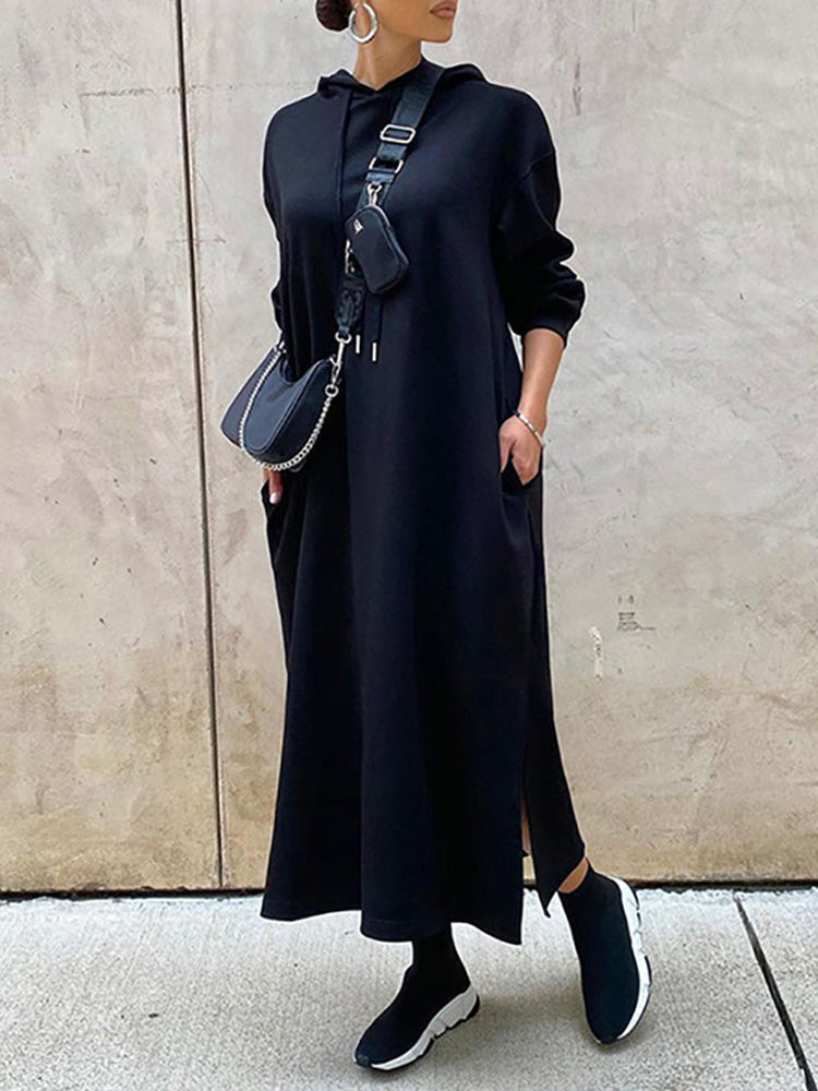 Woman wearing a long black hooded dress with side slits, black socks, and sneakers.