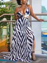 Woman wearing a black and white zebra print maxi dress with a plunging neckline and high slit, standing on a balcony.