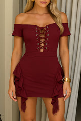 Woman wearing a burgundy off-the-shoulder lace-up mini dress with ruffle and fringe details.