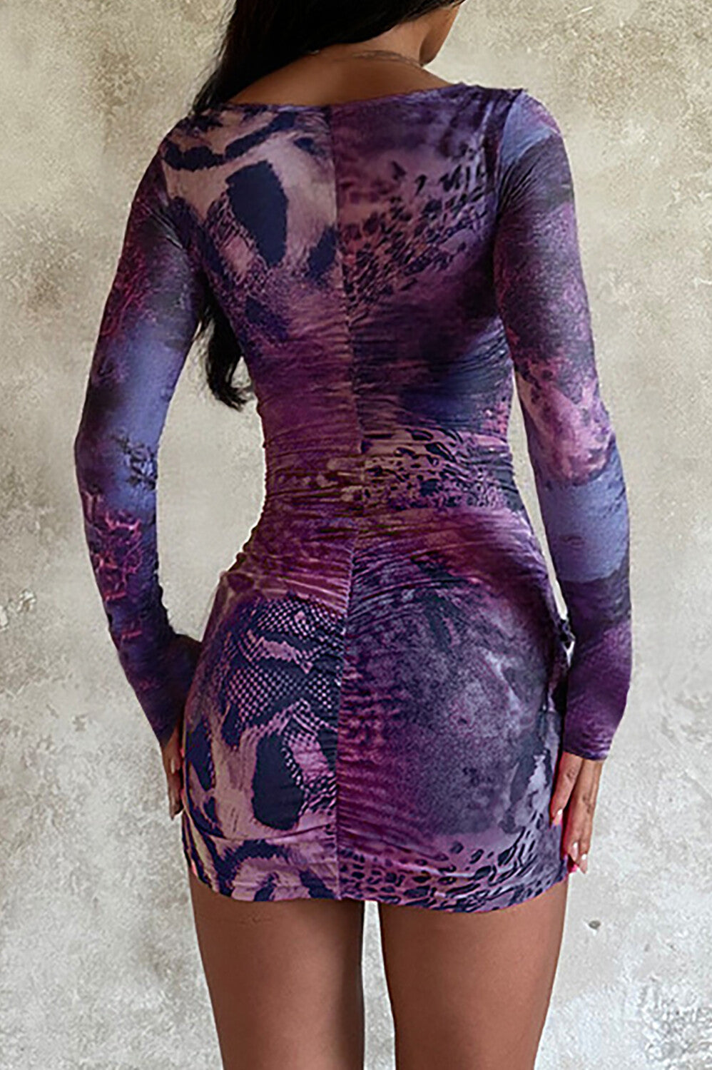 back view of a woman wearing a purple long-sleeved mini dress with a square neckline and ruffled hem