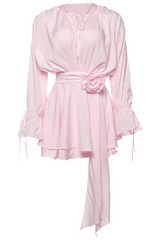 Pink chiffon mini dress with a floral applique at the waist, tie-neck, and ruffled cuffs.
