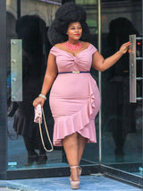 Woman with a large afro hairstyle posing in a pink off-the-shoulder dress with ruffle detail.
