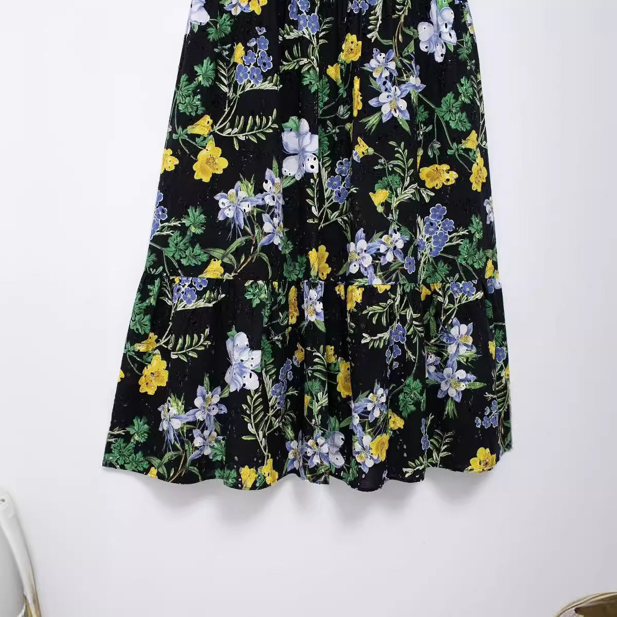 Close-up of the tiered hem and eyelet detailing on a black floral print midi dress