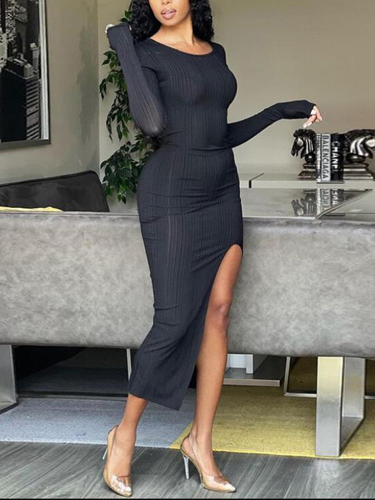 Side profile of a woman in a black long-sleeved ribbed midi dress with a thigh-high slit.