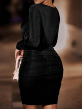 Back view of a woman wearing a black ruched bodycon dress with a halter v-neck and long sleeves.