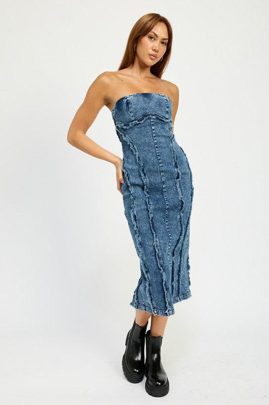 Woman wearing a blue strapless denim midi dress with paneled construction and raw edge detailing, standing against a white backdrop.