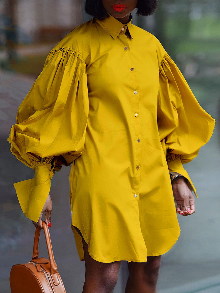 Woman wearing a mustard yellow oversized shirt dress with dramatic balloon sleeves and a round tan handbag.
