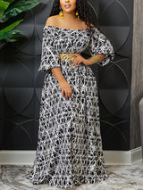Woman wearing a black and white off-the-shoulder maxi dress with a geometric print and a gold belt.
