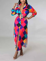 Woman wearing a long, collared shirt dress with a bold geometric print in multiple colors. The dress has long sleeves, a button-down front with a deep V-neckline, a high slit, and is cinched with a wide belt.