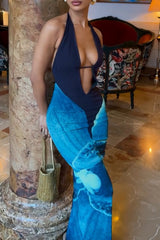 Close-up of a woman's upper body in a navy blue halter maxi dress. The dress has a deep V-neckline and a prominent abstract blue design on the skirt.
