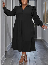 Plus-size model wearing a black tiered midi dress with voluminous sleeves and ruffled shoulders.