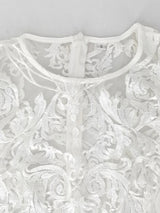 close-up of the neckline and upper chest area of a white lace dress, showing the intricate lace pattern and a zipper closure