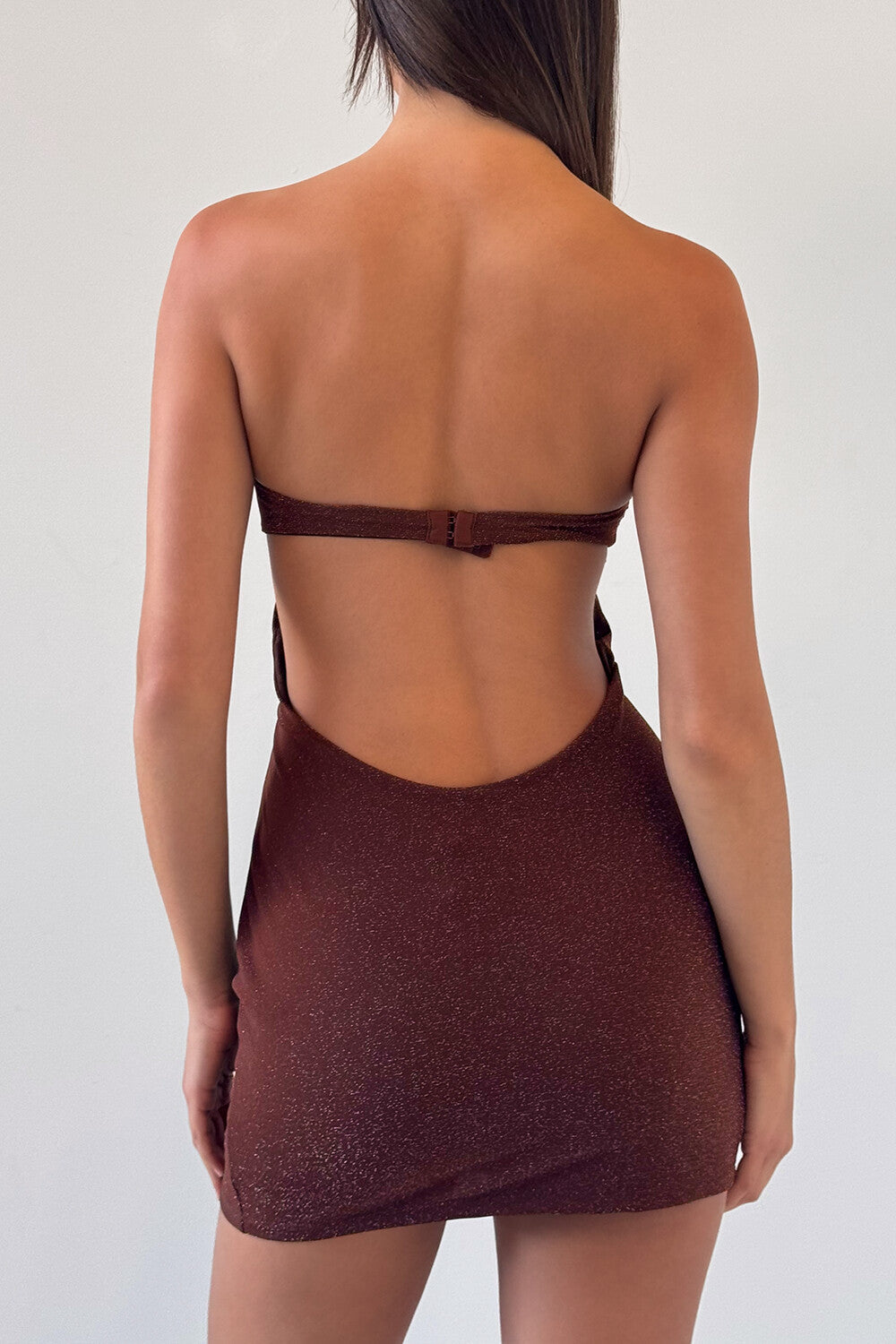 Woman wearing a brown strapless mini dress with a cut-out and ring detail, back view