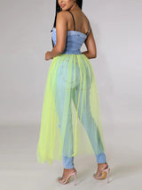 Woman wearing a light blue denim corset top with a long, sheer neon yellow tulle skirt over ripped light blue jeans, back view.