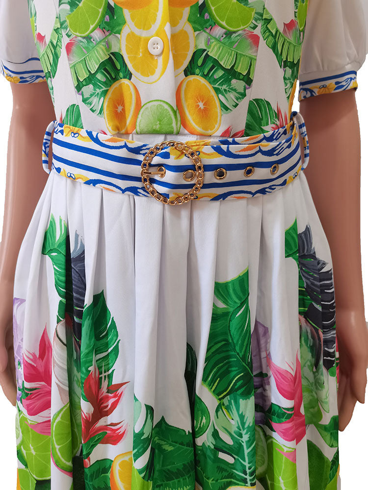 Close-up of the belted waist of a white short-sleeve dress with a tropical fruit and leaf print, featuring a blue and white striped belt with a gold buckle.